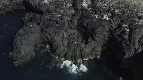 Dark-basalt-cliffs-on-shore-of-Iceland-during-sunny-day,-aerial
