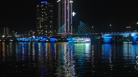 Vista-Nocturna-Cinematográfica-Del-Puente-Tran-Thi-Ly-Sobre-El-Río-Han-Y-Crucero-Navegando-En-La-Ciudad-De-Da-Nang-De-Vietnam-Iluminada-Con-Luces-Y-Edificios-En-El-Horizonte-Al-Fondo