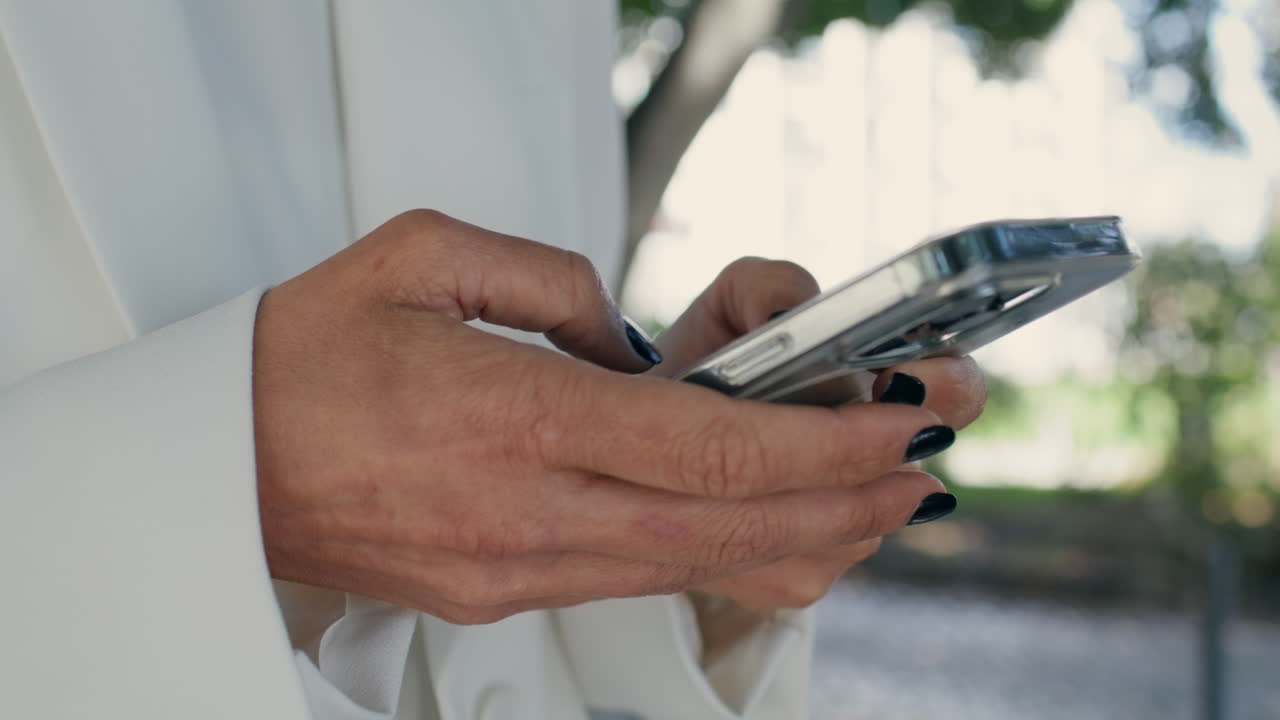 여자 손이 밖에서 스마트폰으로 문자 메시지를 보내고 있습니다. 알려지지 않은 소녀가 전화를 타이핑하고 있습니다.