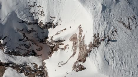 Von-Oben-Nach-Unten-Aufgenommene-Drohnenaufnahme-Eines-Wanderers,-Der-Einen-Schneebedeckten-Bergrücken-Entlang-Läuft-Und-Einen-Steilen-Abhang-überblickt