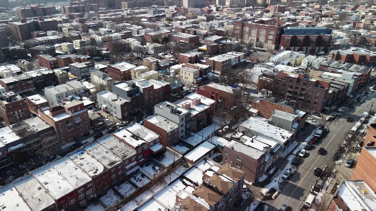 High angle drone footage showing a residential district with snow covered rooftops on a sunny winter day, revealing streets, cars, and the dense urban layout of the city neighborhood
