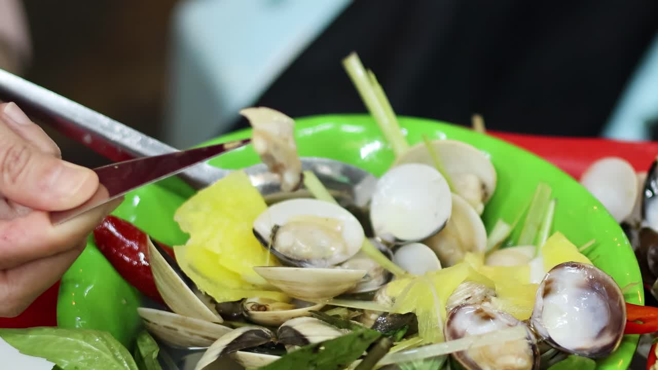 Hands skillfully shuck clams over a colorful salad with fresh greens and vegetables.