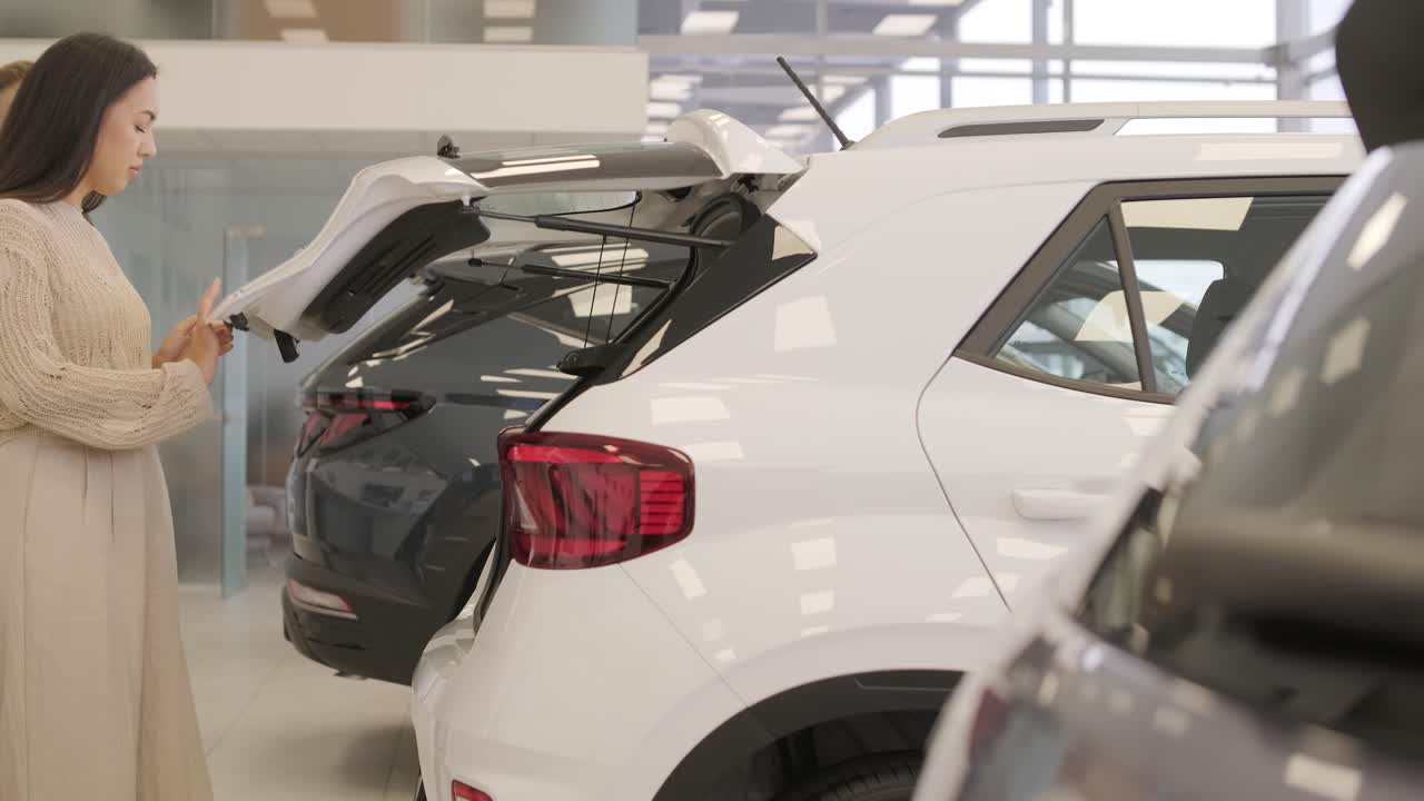 아름다운 젊은 부부는 자동차 전시장에서 새로운 자동차를 선택하고 있습니다.