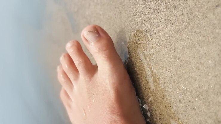 Piede con pedicure scintillante d'oro che allarga le dita nelle pulite onde dell'oceano