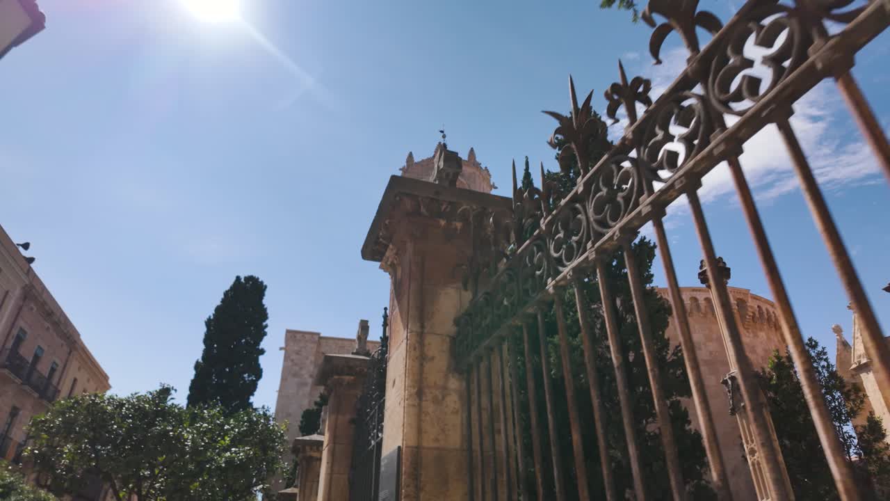 Low angle view of Tarragona Cathedral rising majestically behind ornate railings, bathed in the warm sunlight of a clear Spanish day