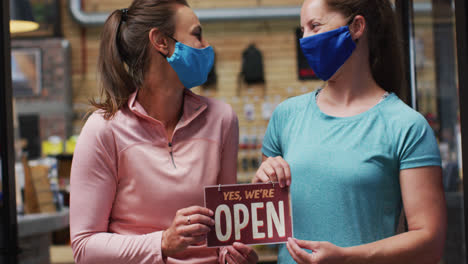 Porträt-Einer-Kaukasischen-Ladenbesitzerin-Mit-Gesichtsmasken-Und-Offenem-Schild-Im-Fenster-Eines-Sportgeschäfts