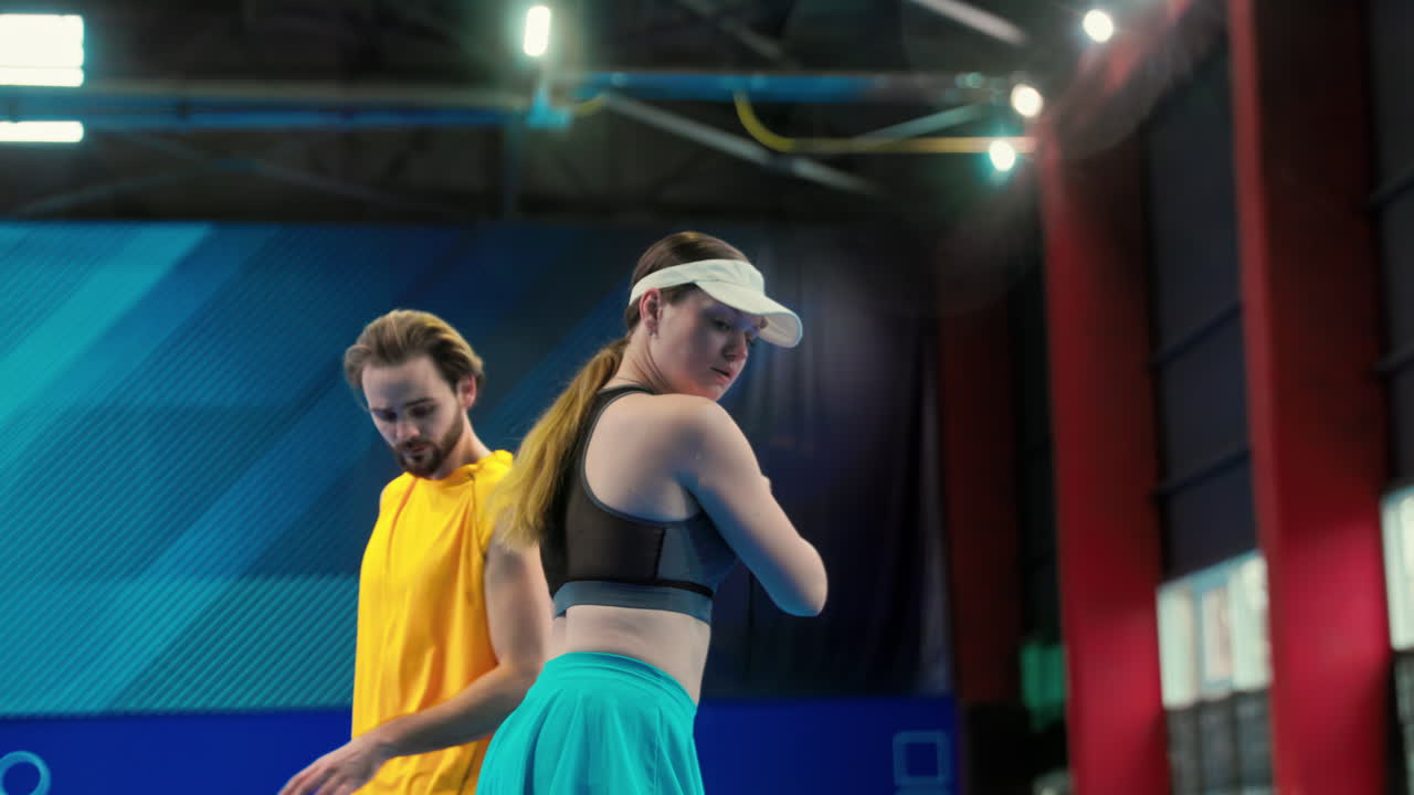 A man teaching a woman how to play pickleball in an inside court