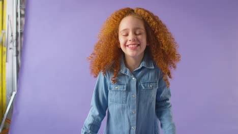 Studio-Portrait-Of-Girl-With-Red-Hair-Laughing-And-Spinning-Against-Purple-Background