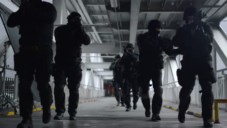 vista frontal de las fuerzas especiales de la policía caminando por el puente metálico de un edificio urbano