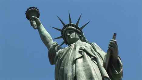 the camera looks up at a towering statue of liberty set against a blue sky