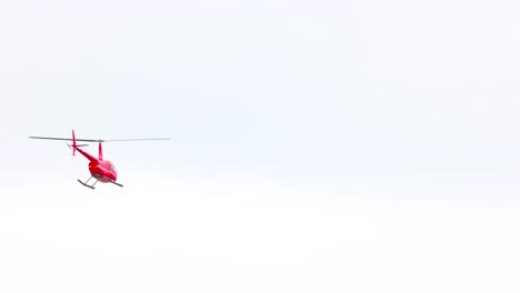a red helicopter gracefully flies over the great ocean road, captured in bright daylight with a clear sky backdrop