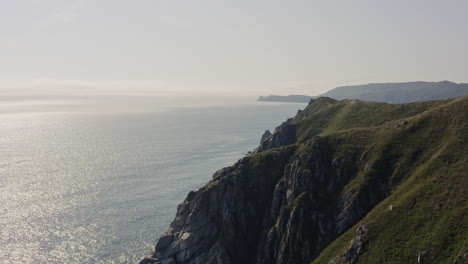 Fly-over-steep-cliff-coasltine-with-deep-blue-ocean-and-a-heavy-dense-fog-approaching-land