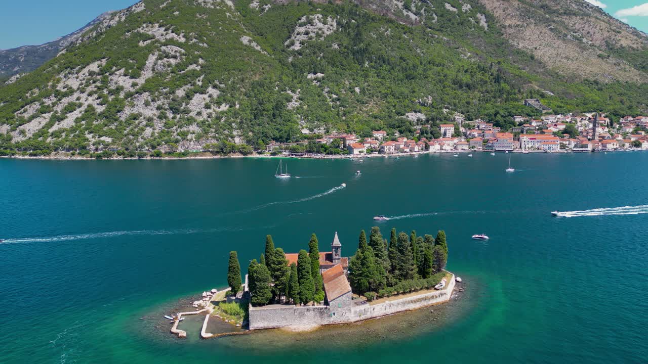 Aerial drone view of Sveti Dorde Island - Saint George Monastery in the middle of the island. In background is Perast city. Famous travel destination in Montenegro. Drone forward, descending.