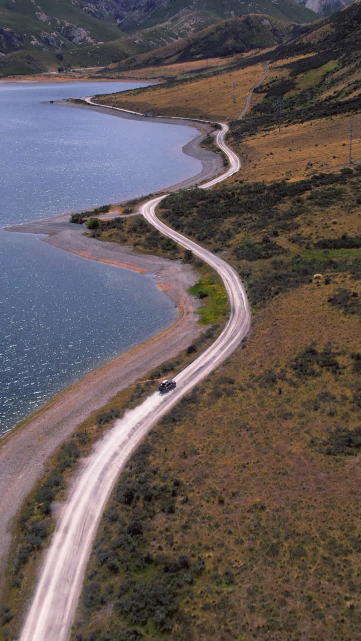 Vertical drone shot following a car driving at Lake Lyndon in sunny New Zealand