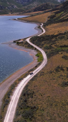 vertical drone shot following a car driving at lake lyndon in sunny new zealand