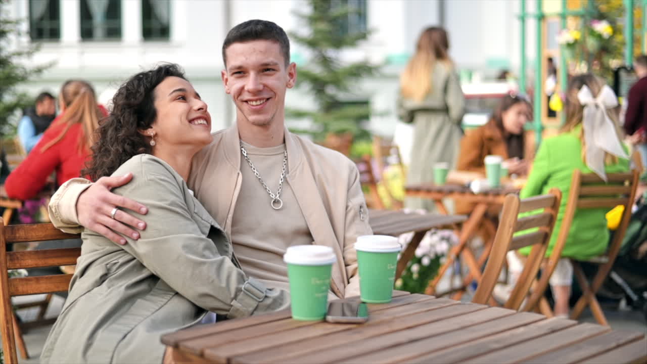 Una coppia felice all'aperto vicino a un bar. Si abbracciano, sorridono, caffè. Atmosfera autunnale. Movimento al rallentatore