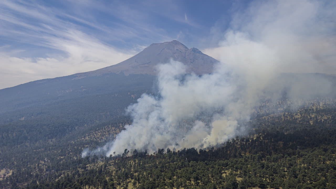 Drone footage captures a forest fire spreading near Popocatépetl Volcano in central Mexico, with thick smoke rising over pine-covered slopes.
