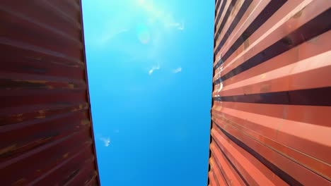 looking up between shipping containers: a unique perspective on industrial design and urban landscape against a clear blue sky