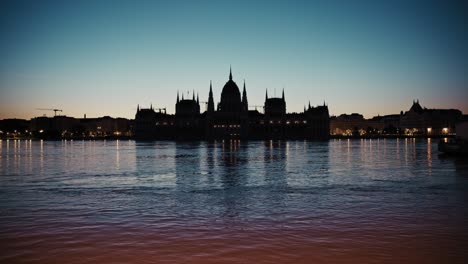 silhouette of budapest’s parliament building at dusk with floodwaters reflecting city lights