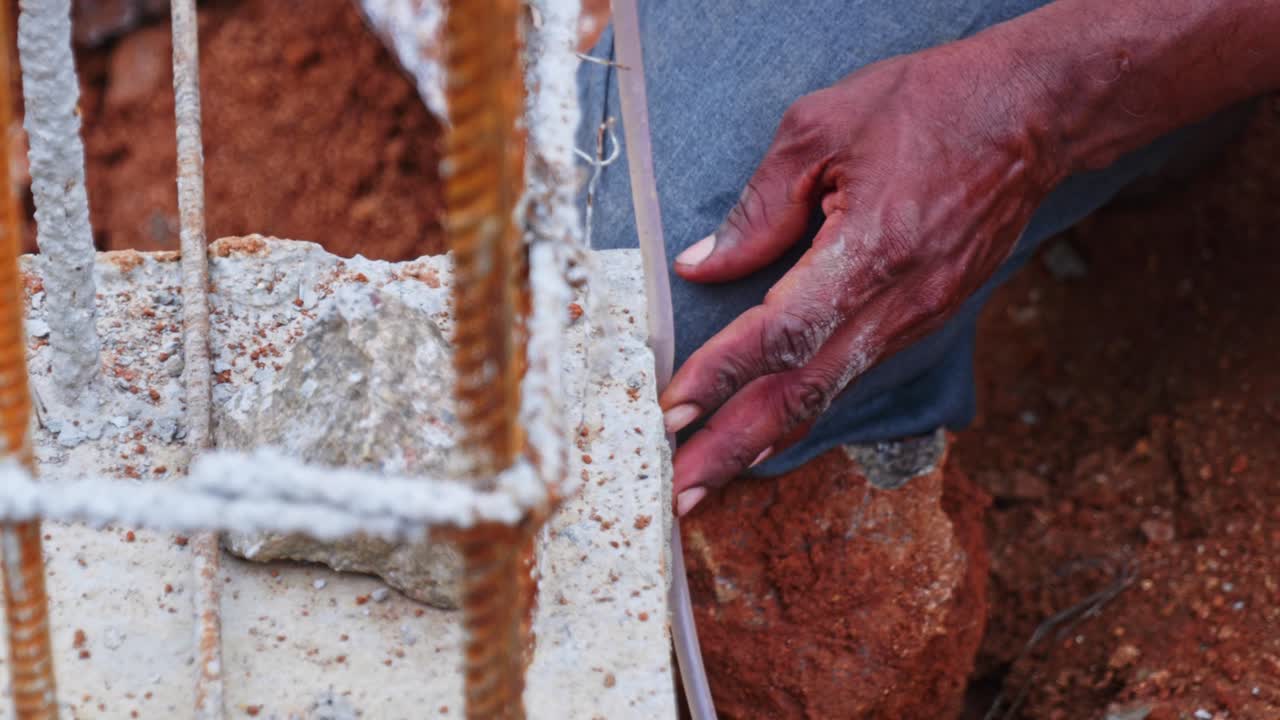 Operaio edile che usa un tubo a livello d'acqua per l'allineamento delle fondamenta in un cantiere a Hyderabad, Telangana, India. Di giorno, ripresa stabile, 4k.