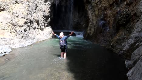 turista mochilero camina por el río y levanta los brazos en señal de logro