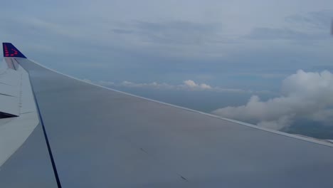 wing of an airplane seen from window flying high above clouds with a clear sky in the background