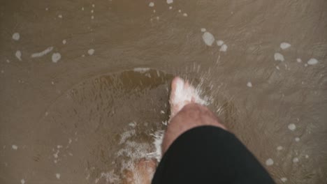 a man walking along a beach as the water laps at his feet