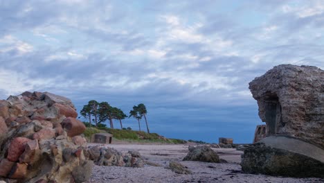 Beautiful-vibrant-sunset-time-lapse-of-fast-moving-clouds-over-the-Baltic-sea-coastline-at-Liepaja,-dark-storm-clouds,-old-fortification-ruins-in-foreground,-calm-sea,-copy-space,-low-angle-wide-shot