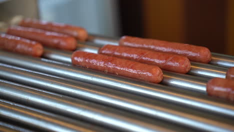 close up of sausages rolling on a hot dog grill machine in fast-food diner