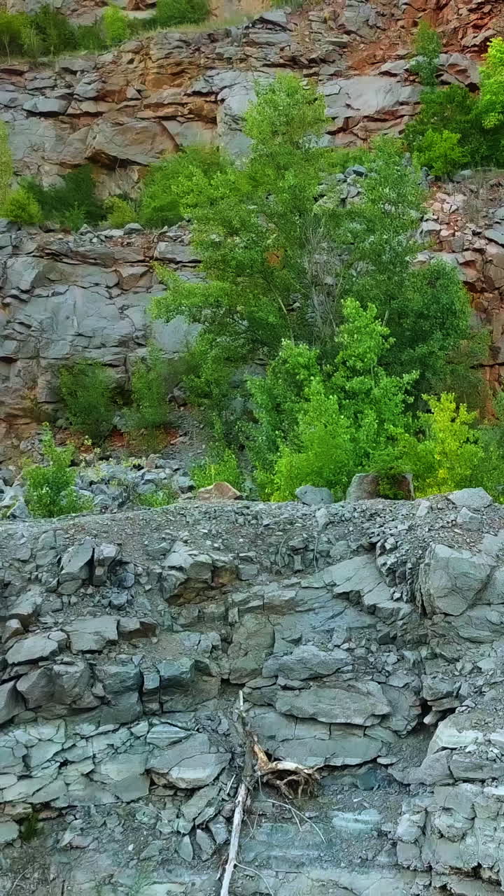 A tourist with a backpack walks around the lake on the background of a quarry on a warm day. Gray background. Camera motion to right. Vertical video