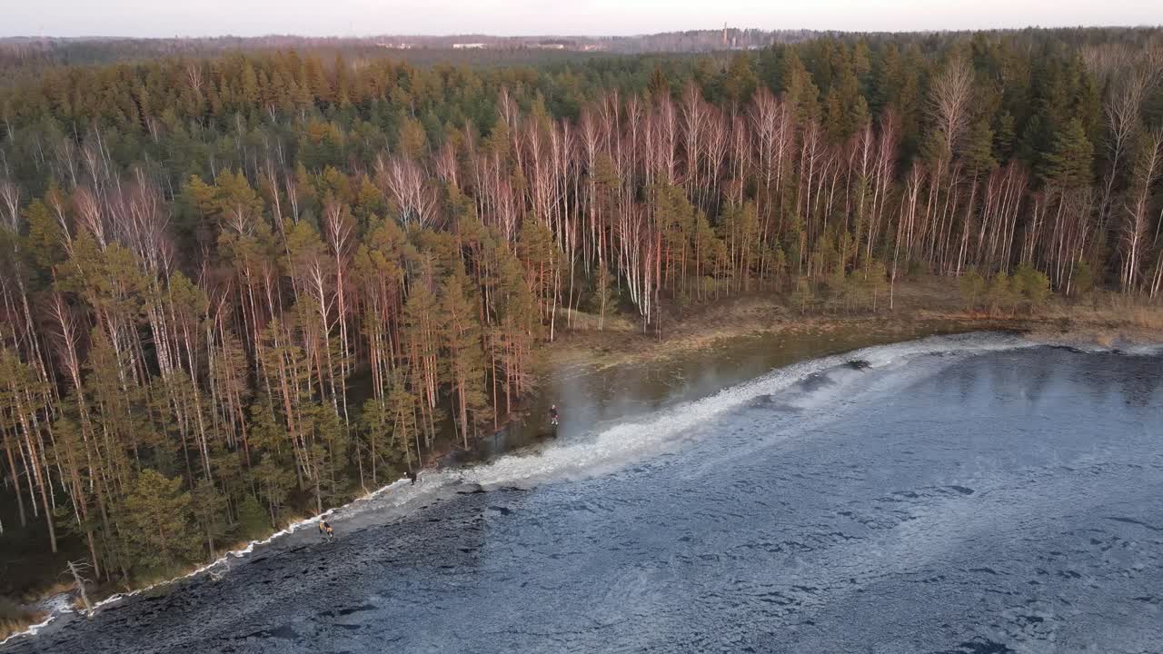 persone che pattinano su un lago circondato da una lussureggiante foresta invernale