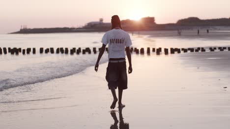 Ein-Afrikanischer-Mann,-Männlich,-Mann,-Modell,-Junge-Geht-Am-Strand-Entlang,-Meereswasser-Im-Sonnenuntergang-Mit-Wellen