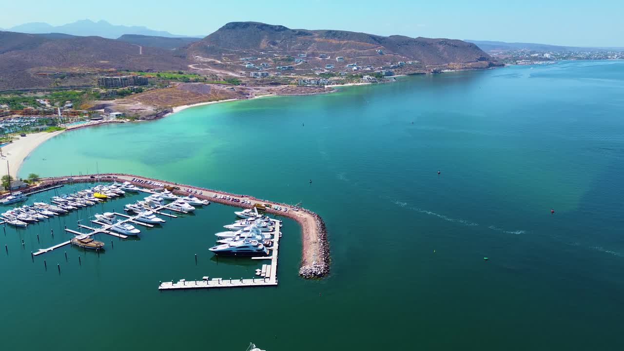 Vista panorâmica de uma marina com barcos, cenário oceânico e campo de golfe adjacente, destacando o estilo de vida costeiro em La Paz, Baja California Sur, México