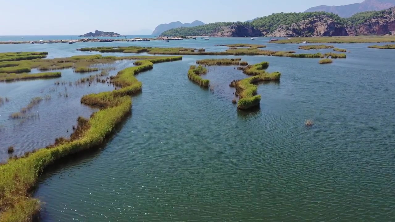 Panoraamainen korkea ilmakuva Dalyan-joen suiston kultaisten ruovikkojen ja sinisten vesikanavien labyrintista, jota kehystävät vuoret Muglassa, Turkissa.