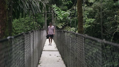 El-Turista-Camina-Sobre-El-Puente-Colgante-En-La-Cámara-Tropical-De-La-Selva-Tropical-En-La-Mano