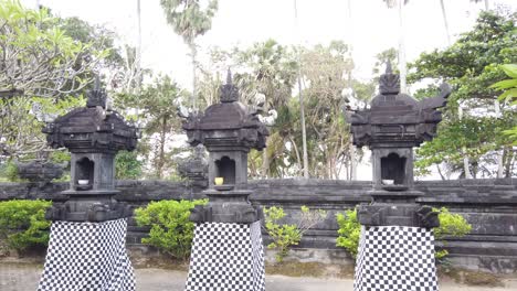 Balinese-Temple-Architecture-with-Black-and-White-Clothes-Displayed-in-Outdoors-Court,-Trees-and-Plants-at-Pavilion-of-Anyar-Saba,-Gianyar