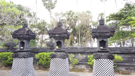 balinese temple architecture with black and white clothes displayed in outdoors court, trees and plants at pavilion of anyar saba, gianyar