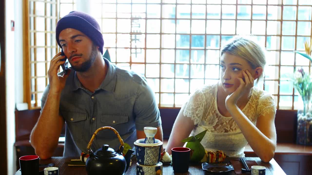 남자가  ⁇ 드폰으로 이야기하는 동안 여성이 지루해지고 있습니다.