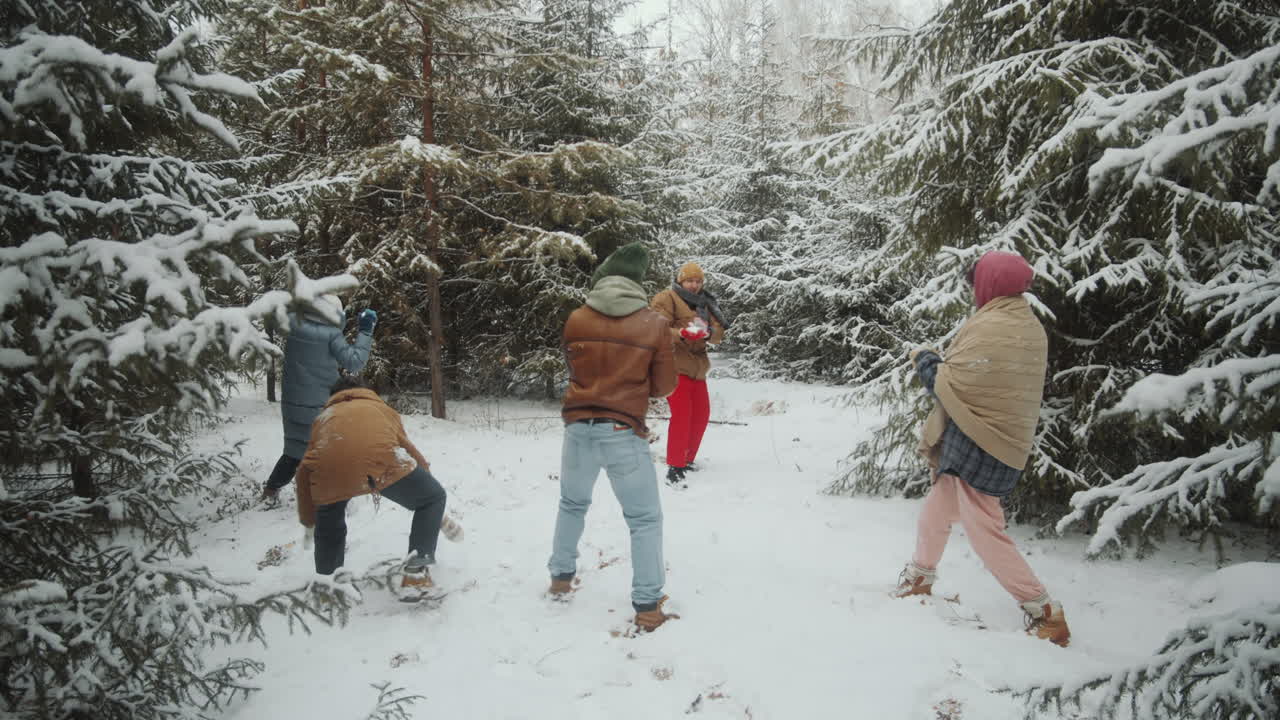 amigos jóvenes teniendo una pelea de bolas de nieve en el bosque de invierno
