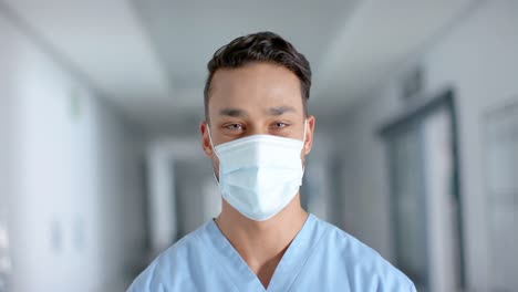 Portrait-of-happy-biracial-male-doctor-wearing-face-mask,-slow-motion