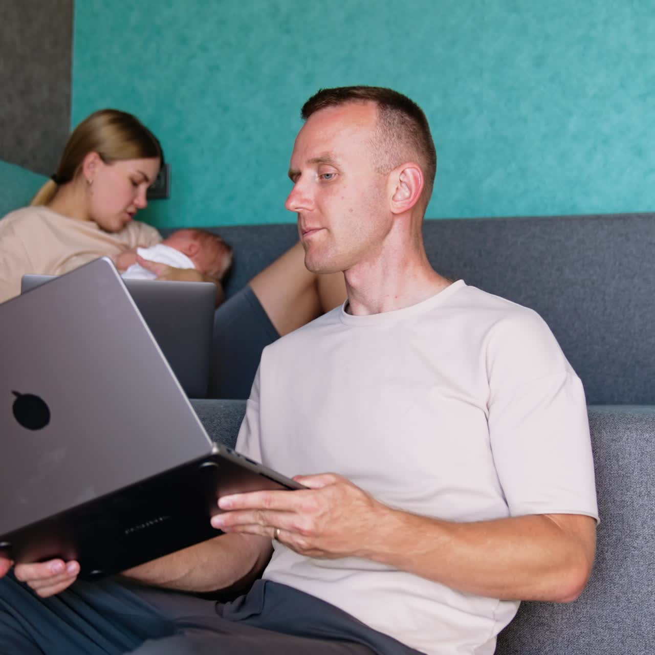 En travl mor med en nyfødt baby skal tage sig af barnet og arbejde. Manden sidder i sofaen og er fuldt fokuseret på sit arbejde på sin laptop og spørger sin kone om problemer på computeren.