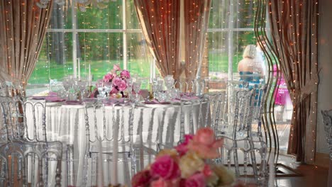 shot of fancy wedding reception tables with glasses and plates, table is decorated with gorgeous pink and white roses and white candles, panning shot