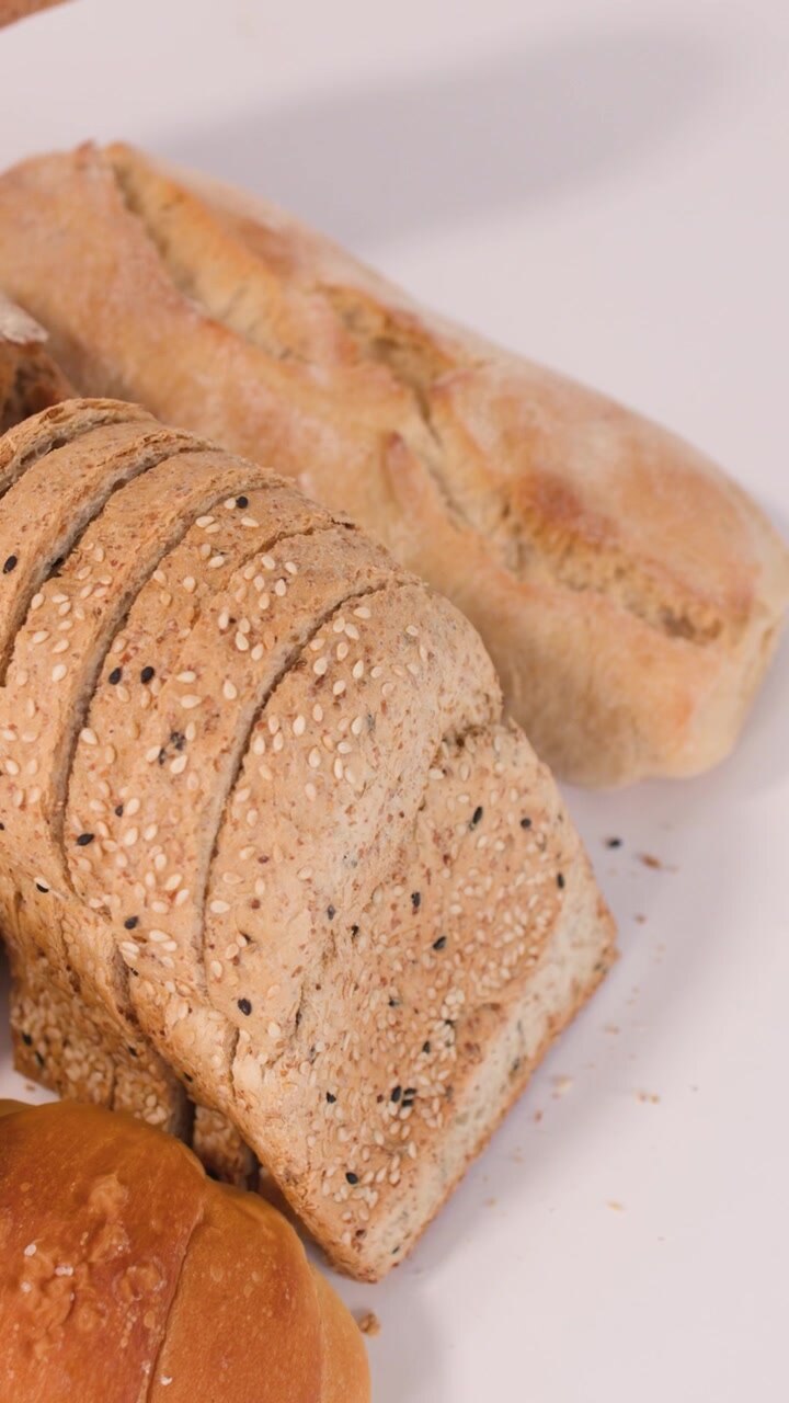 Close-up panning shot of sourdough, baguettes, croissants, and sliced grain bread on white surface.
