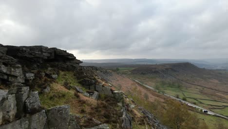 Aerial-drone-footage-revealing-a-dramatic-rock-formation-and-large,-open-fields-in-the-Peak-District-UK