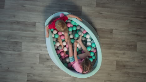 little brother and sister sit in dry pool with colored balls