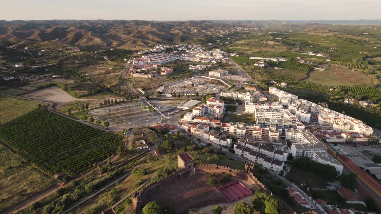 Voo panorâmico amplo do Castelo de Silves envolto no dourado do anoitecer, Algarve, Portugal.