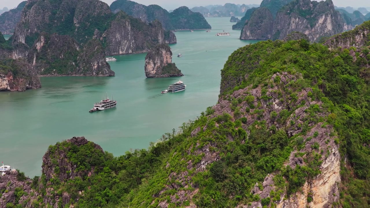 Vịnh Hạ Long Việt Nam: Cảnh quay dolly từ trên không các tàu du lịch đi qua những ngọn núi đá vôi karst tươi tốt với đàn chim bay lượn