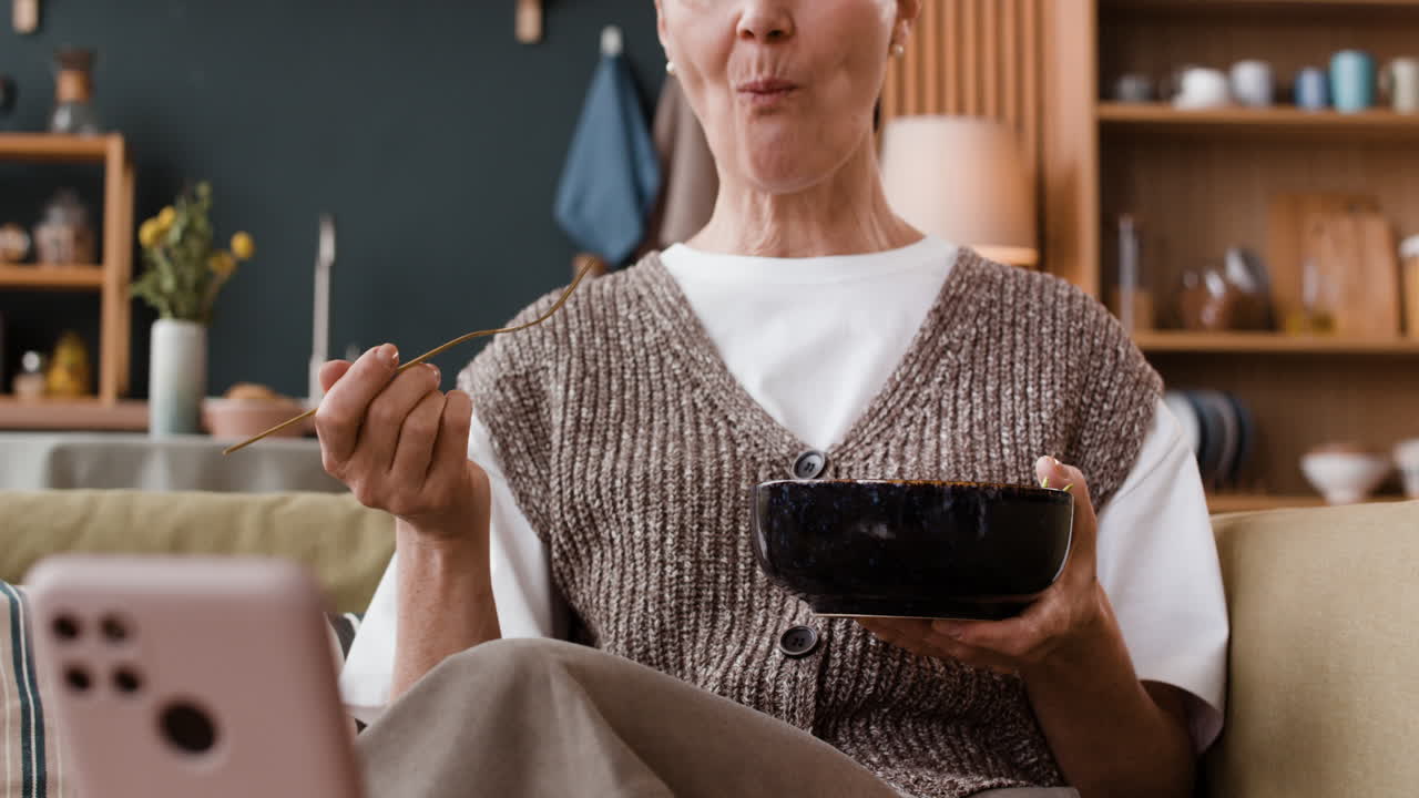 Person eating while looking at a smartphone on a couch