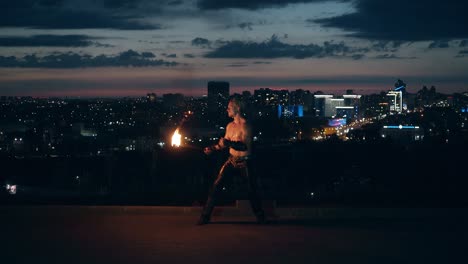 Young-blond-male-does-tricks-with-fire-breaths-fireball-in-the-middle-of-the-night-with-city-skyline-in-background-1