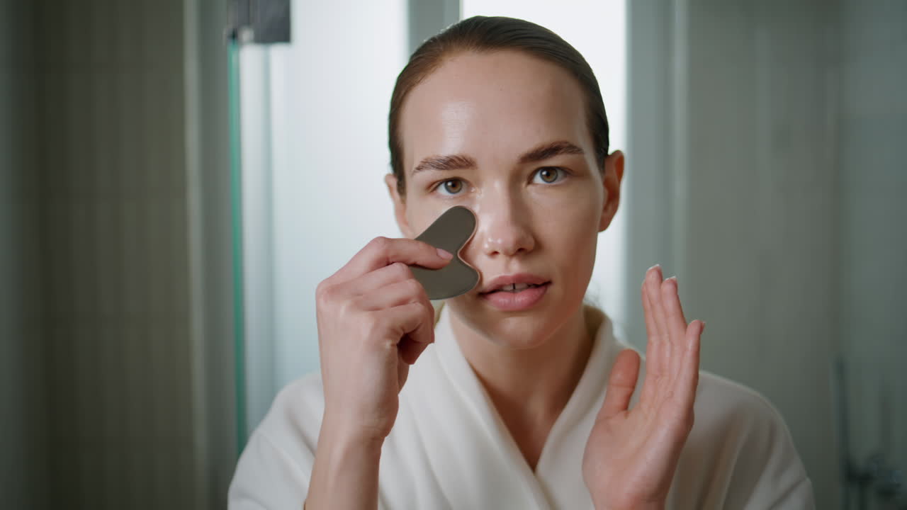 Young woman massaging face with gua sha. Closeup girl do stone treatment at home